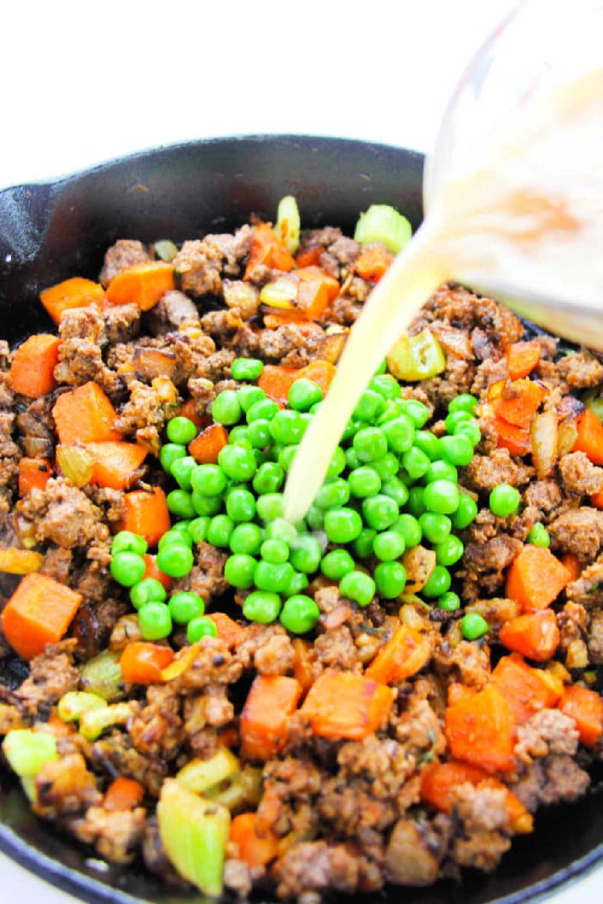 Ground beef, diced carrots, celery, and peas sizzle in a skillet as broth is poured over the mixture—the perfect filling for a classic Shepherd's Pie with Instant Potatoes.