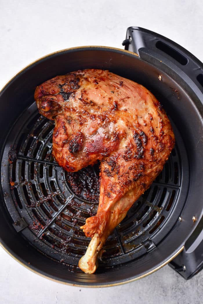 Cooked turkey leg quarters recipe with crispy skin in an air fryer basket on a light background.