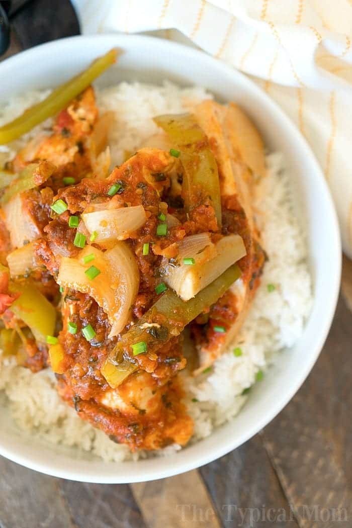 Salsa chicken crockpot recipe that only requires a few ingredients and is a healthy slow cooker dinner for sure! Shred it and make tacos or serve it on top of rice for a delicious meal packed with vegetables. If you need an easy family friendly dinner that is inexpensive but super flavorful this is it. #crockpot #slowcooker #salsachicken #chicken #healthy #salsa #crockpotrecipes #thetypicalmom A bowl of white rice topped with slow cooker salsa chicken, bell peppers, onions, and chopped green herbs.