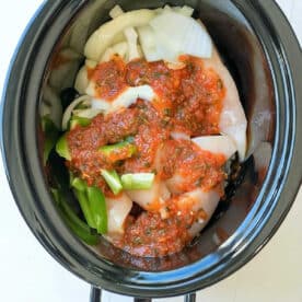 Chicken, onions, bell peppers, and tomato sauce in a black slow cooker, perfect for an easy salsa chicken crockpot recipe.