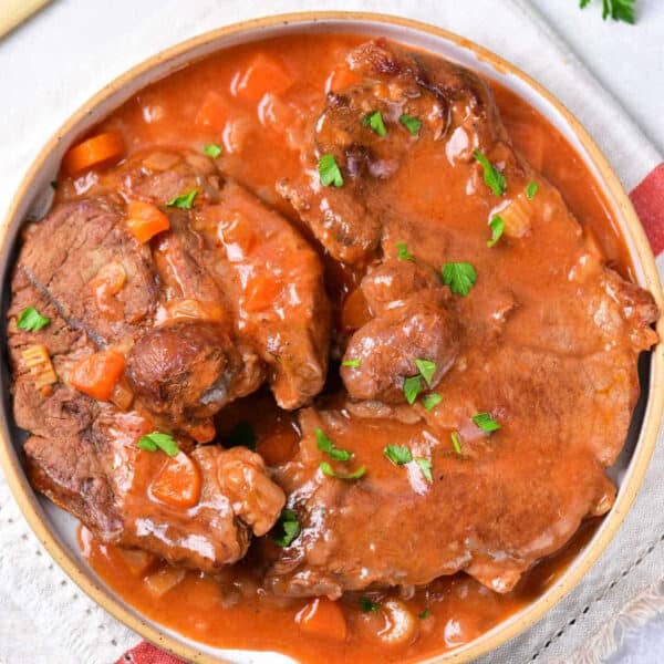 A bowl of braised beef in tomato sauce, garnished with chopped parsley, on a cloth napkin—just like you’d enjoy after learning how to cook beef shin in oven for tender, flavorful results.
