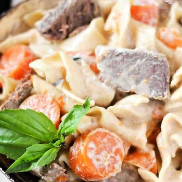 A bowl of creamy crockpot beef stroganoff and noodle stew with carrots, garnished with fresh basil.