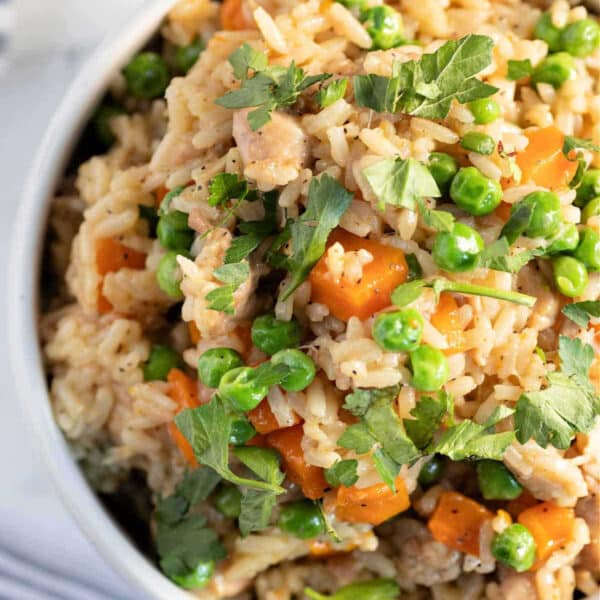 A bowl of instant pot chicken thighs and rice with peas, carrots, herbs, and pieces of meat, garnished with fresh parsley.