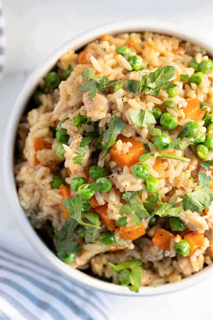 A bowl of instant pot chicken thighs and rice with peas, carrots, herbs, and pieces of meat, garnished with fresh parsley.
