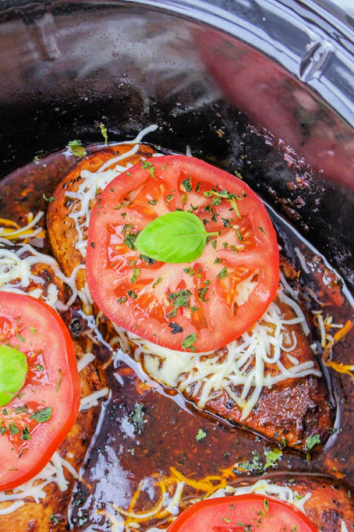 Crockpot Chicken Frozen Breasts topped with melted cheese, tomato slices, and basil simmer in a slow cooker with savory sauce.