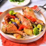 Plate of crispy roasted chicken drumsticks with mixed vegetables on an orange napkin, offering a delightful hint of how long to cook chicken legs in the air fryer for that perfect crunch.