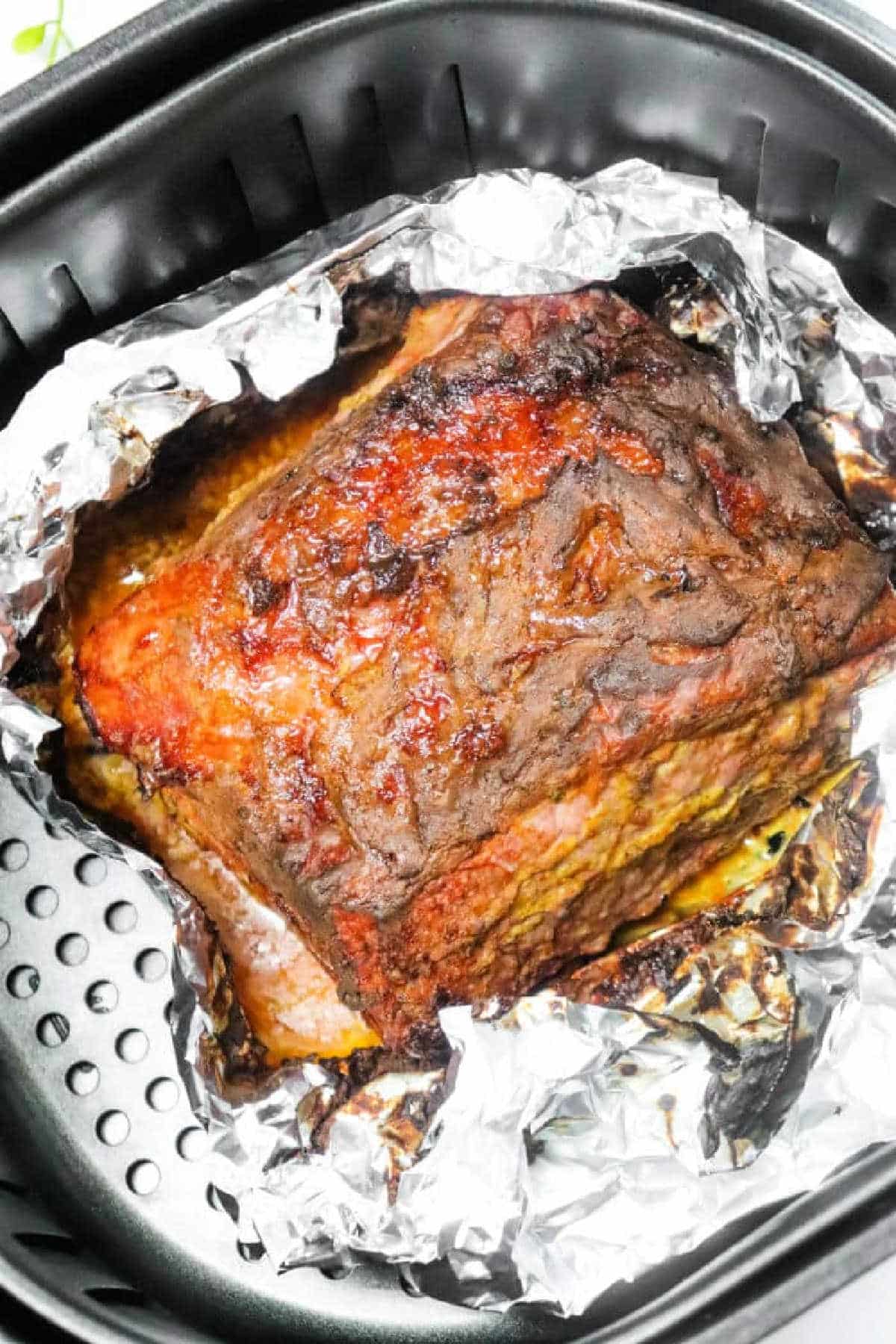 Cooked Air Fryer Corned Beef resting on crumpled aluminum foil inside an air fryer basket.