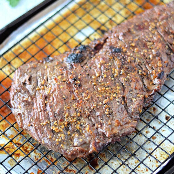 A cooked, seasoned skirt steak in oven rests on a wire rack over a baking sheet, with parsley leaves nearby.