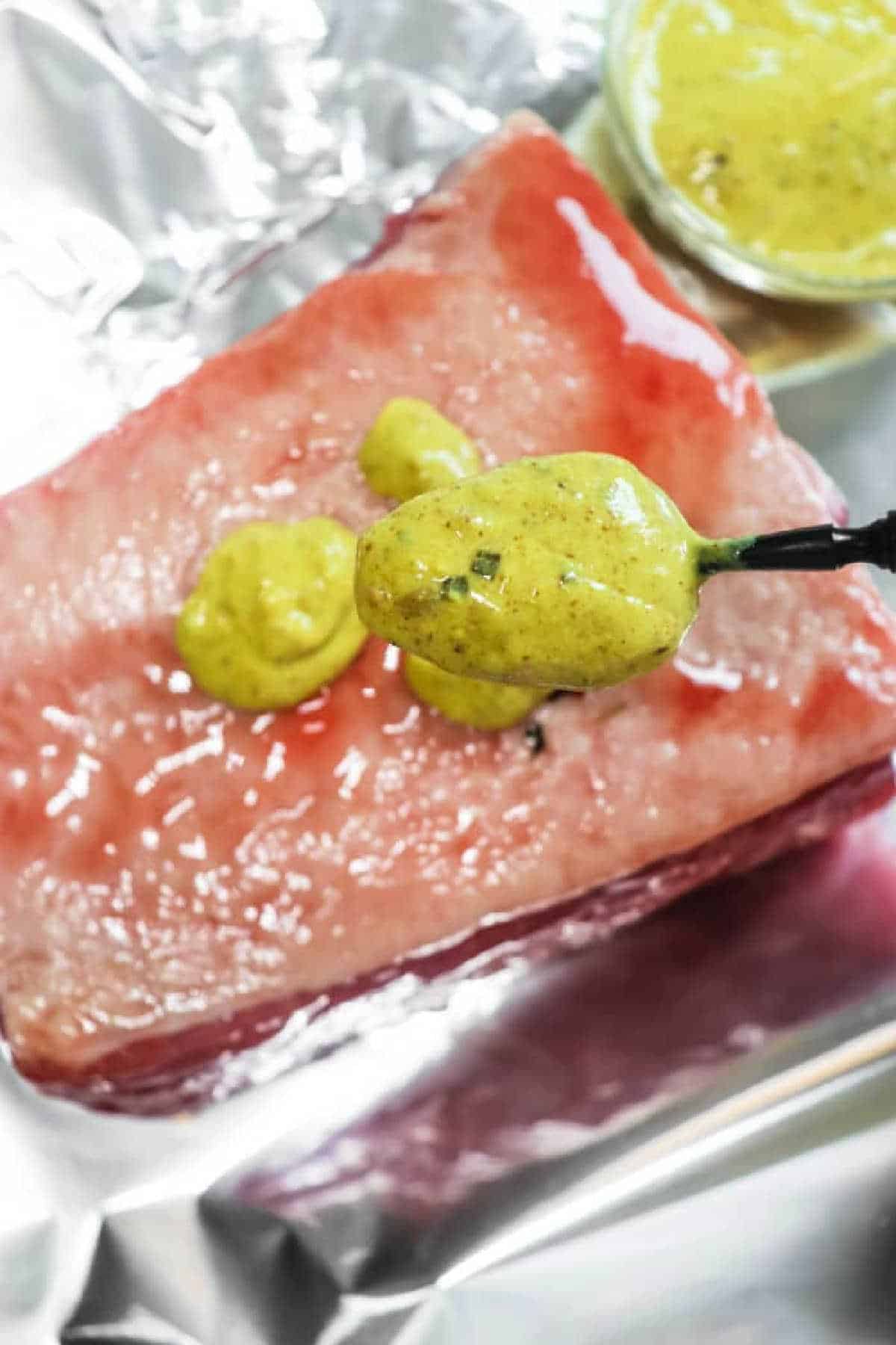 A spoon spreads yellow mustard sauce onto a raw corned beef brisket on aluminum foil, perfect for making Air Fryer Corned Beef.