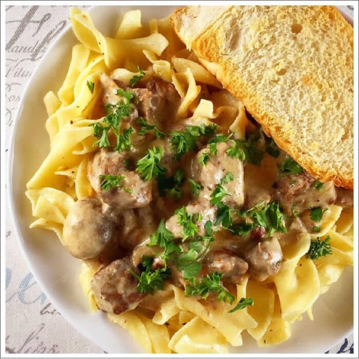 Crockpot beef stroganoff that only requires 5 ingredients and cooks all day in the crockpot. The best way to make tender beef with a creamy sauce. #crockpot #slowcooker #beefstroganoff #beef #stew A plate of creamy crockpot beef stroganoff over egg noodles, topped with parsley and served with a slice of bread.