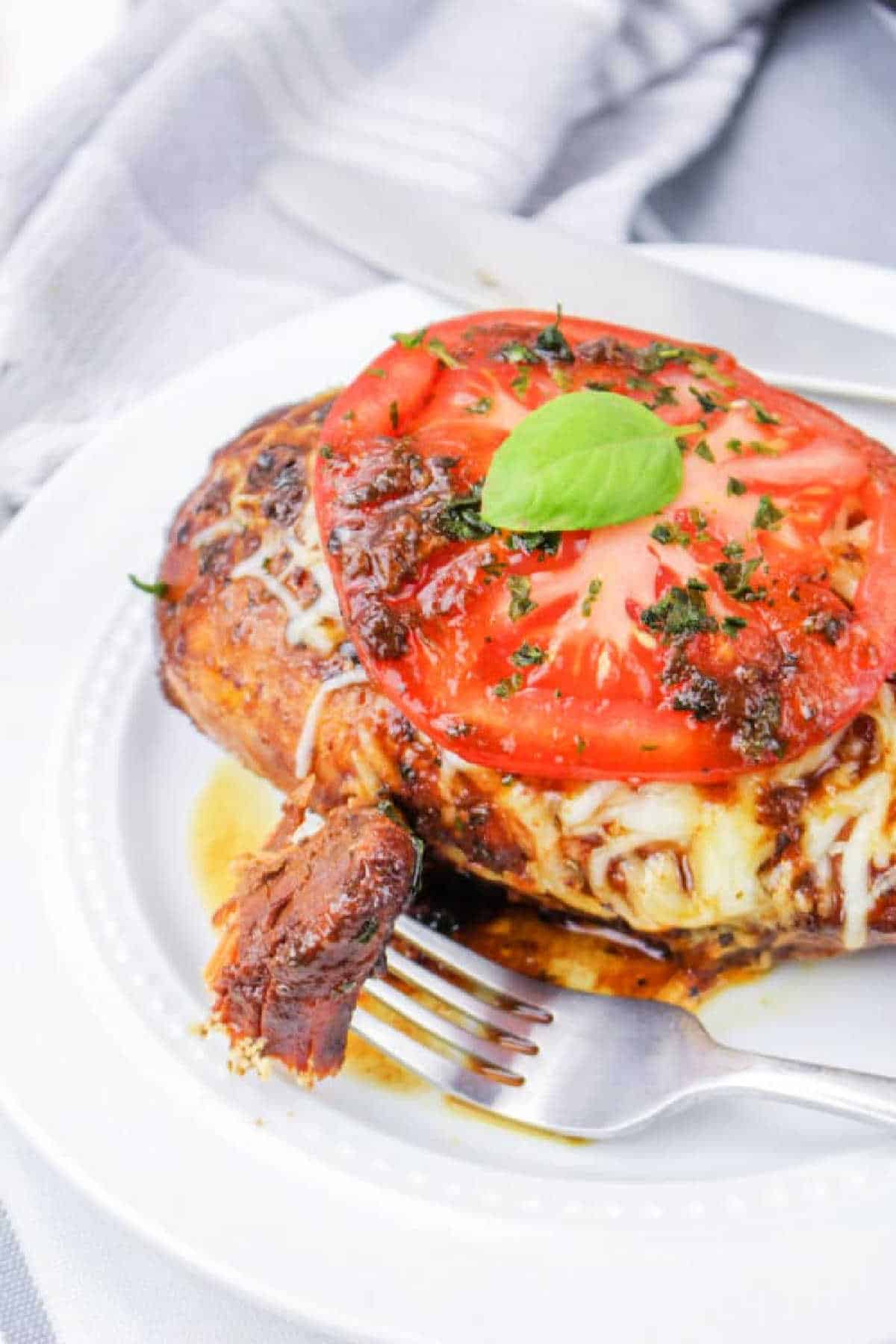 Crockpot Chicken Frozen Breasts are transformed into balsamic chicken breast, topped with melted cheese, fresh tomato slices, and basil on a white plate.