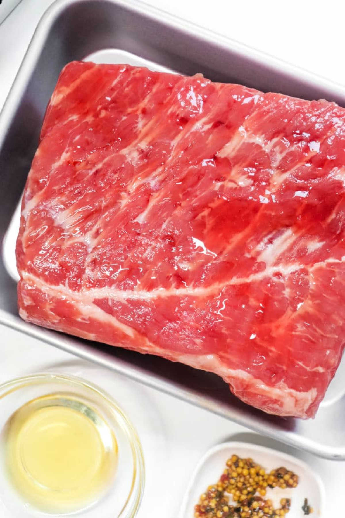 Raw beef short ribs in a metal tray, with a small bowl of oil and spices nearby—perfect for preparing alongside Air Fryer Corned Beef for a flavorful meal.