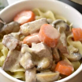 A bowl of creamy Instant Pot beef stroganoff with stew meat, carrots, mushrooms, and noodles.