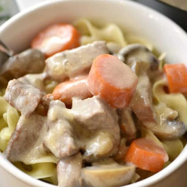 A bowl of creamy Instant Pot beef stroganoff with stew meat, carrots, mushrooms, and noodles.