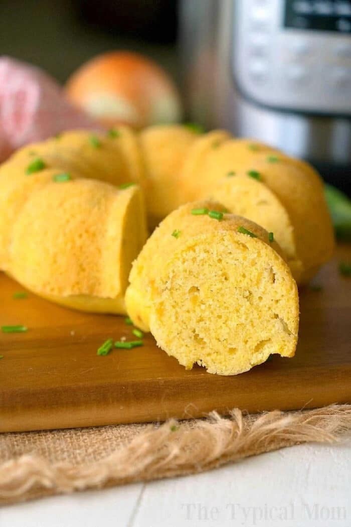 Pressure cooker cornbread is the perfect side dish for any holiday and perfect served with chili! An easy homemade cornbread recipe cooked right in your Instant Pot and comes out so pretty using this bundt pan. #pressurecooker #instantpot #cornbread #instantpotrecipes #homemade #bundtcake #sidedish #bread #thetypicalmom A sliced pressure cooker cornbread ring garnished with chopped chives rests on a wooden board.