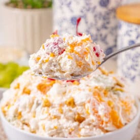 A spoonful of creamy fruit salad held above a bowl filled with the same salad, showcasing this easy ambrosia recipe.