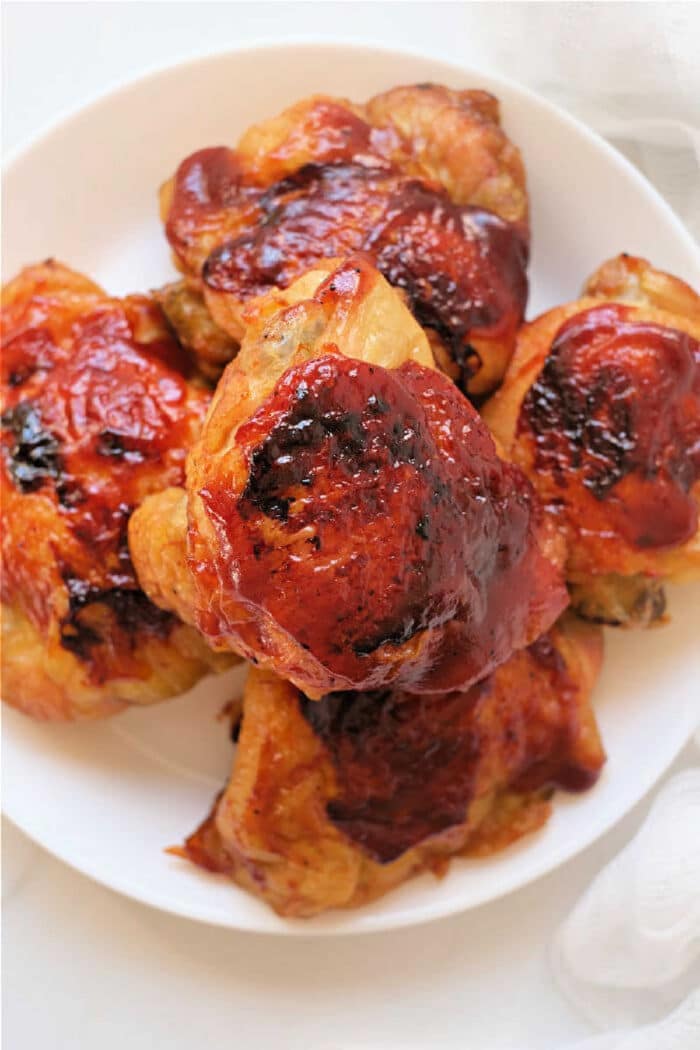 Plate of baked chicken thighs with a shiny, reddish-brown barbecue glaze on top—an easy dish to recreate using frozen chicken thighs in the air fryer for quick, delicious results.