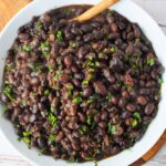 A bowl of black turtle beans cooked to perfection, garnished with chopped herbs, and elegantly served with a wooden spoon. Discover how to cook these delightful beans and elevate your culinary experience.