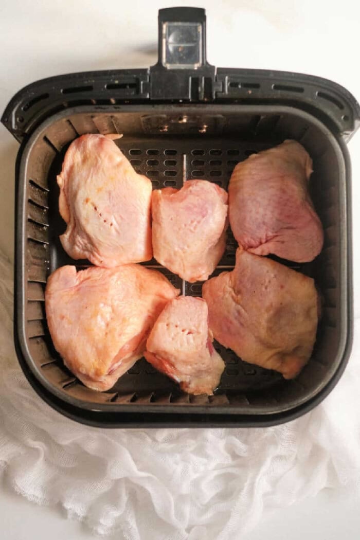 Six raw or frozen chicken thighs placed inside an air fryer basket, ready to be cooked for a quick and easy meal.