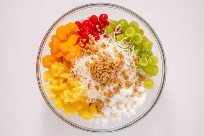 Easy ambrosia recipe for you that just takes a few ingredients and is really yummy. Dessert side dish with fruit and marshmallows our whole family loves. #ambrosia #salad #fruit #sidedish #marshmallow Glass bowl with grapes, pineapple, mandarin oranges, cherries, marshmallows, shredded coconut, and chopped nuts—an easy ambrosia recipe perfect for any occasion.