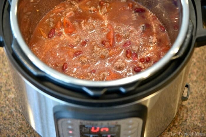 Instant Pot chili mac recipe that takes 5 minutes to cook and you and your kids will love! A classic old fashioned goulash dinner packed with flavor. #instantpot #chilimac #chili #macaroni #goulash #pressurecooker #groundbeef #instantpotrecipes #thetypicalmom Chili with beans and tomatoes cooking in an Instant Pot on a kitchen counter, perfect for trying out your favorite instant pot chili mac recipe.