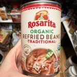 In a well-stocked pantry, a hand grasps a can of Rosarita organic traditional refried beans, ready to unveil how to make canned refried beans better with a few simple tips.