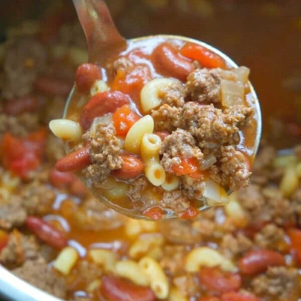 A ladle of goulash with ground beef, macaroni, kidney beans, and tomato sauce is served over a pot—just like an instant pot chili mac recipe.