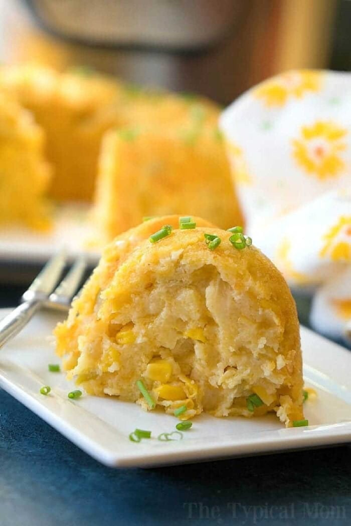This Instant Pot corn casserole recipe is a must during the holidays. Cheesy creamed corn side dish in your pressure cooker for Thanksgiving is a must! #corncasserole #instantpot #instantpotrecipes #thetypicalmom #casserole #thanksgiving #pressurecooker #corn A slice of cornbread with corn kernels, inspired by an instant pot corn casserole recipe, topped with chopped chives, on a white plate with a fork.