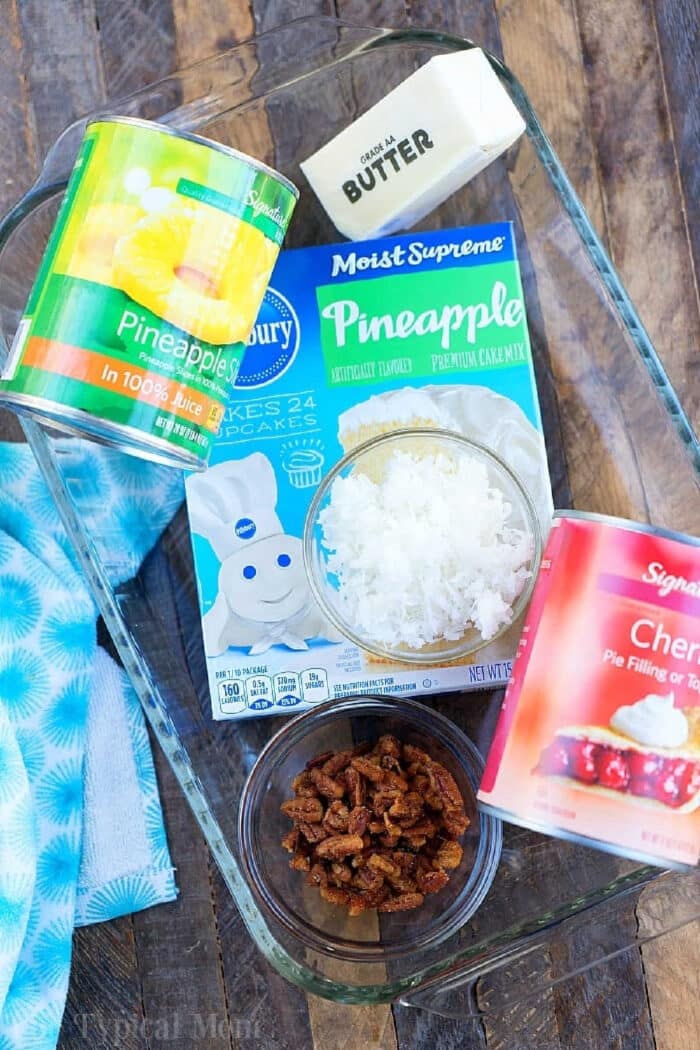 Pineapple cherry dump cake recipe turns out amazing! A fruit dessert with only 4 main ingredients and you can add to it like coconut and nuts too. #pineapple #cherry #dumpcake #cake #cake #coconut #dessert Glass dish layered with canned pineapple, cherry pie filling, cherry pineapple dump cake with white cake mix, shredded coconut, butter, and chopped pecans.