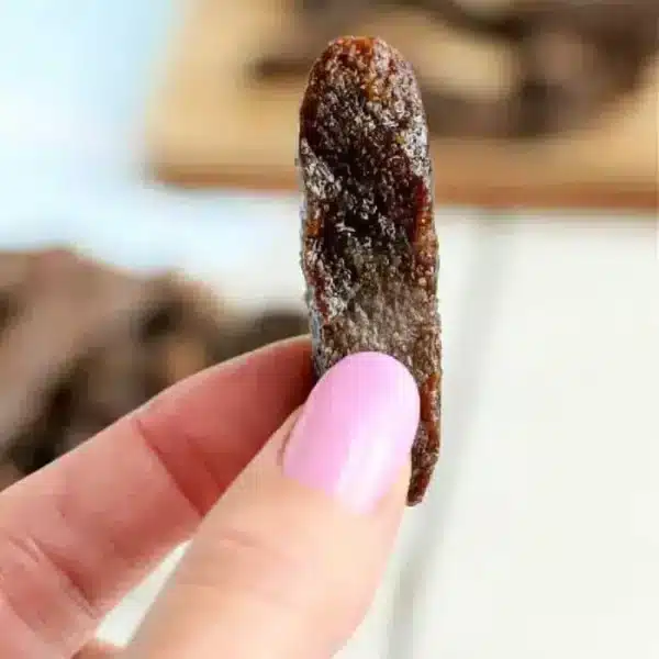 A hand holding a piece of air fryer beef jerky