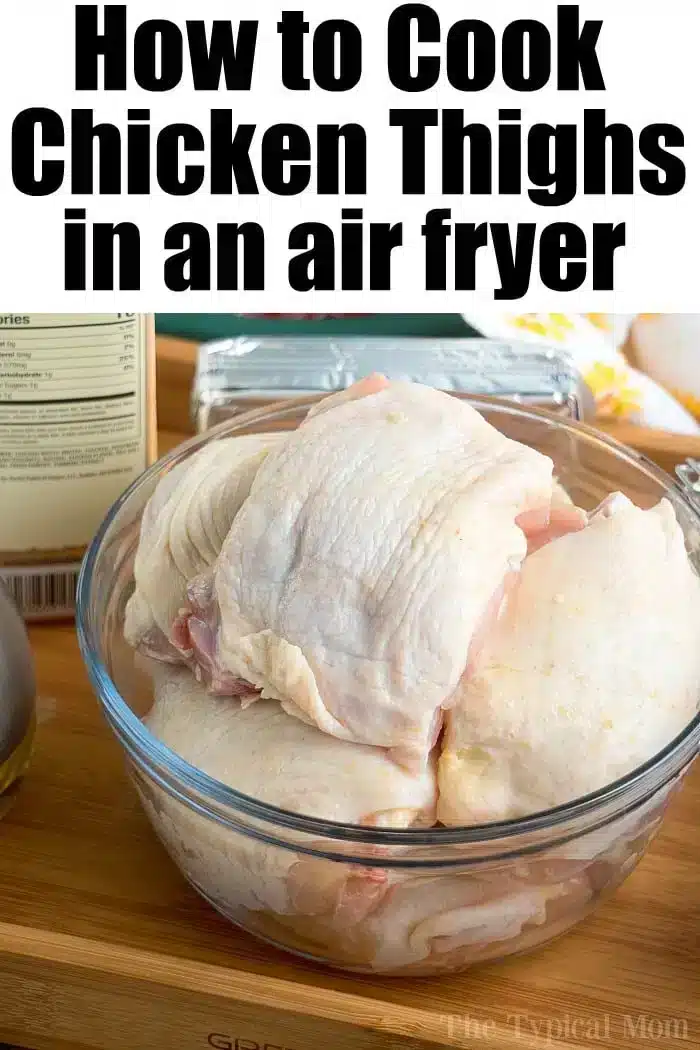 A clear glass bowl filled with raw bone-in chicken thighs is placed on a wooden surface. Behind the bowl, there is a package of butter, a bottle of olive oil, and other kitchen items. The text at the top reads "How to Cook Chicken Thighs in an Air Fryer.