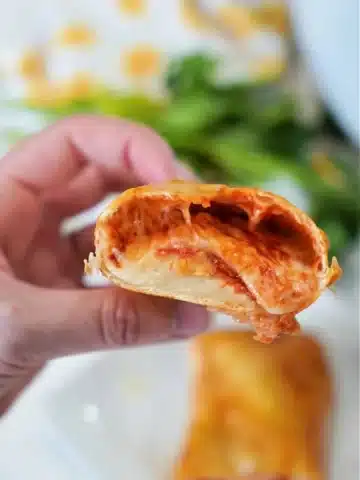 A hand holding half of a stuffed, golden-brown baked tortilla, with melted cheese and a tomato filling visible.