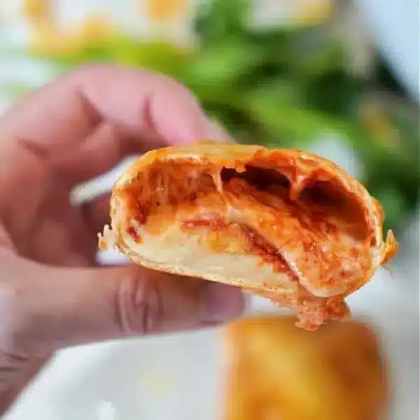 A hand holding half of a stuffed, golden-brown baked tortilla, with melted cheese and a tomato filling visible.