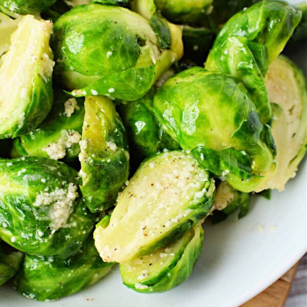 A close-up of boiled Brussels sprouts seasoned with herbs and crumbled cheese on a white plate, ready in just the right amount of time to achieve their perfect tenderness. Knowing how long to boil Brussels sprouts enhances their flavor, making every bite delightful.