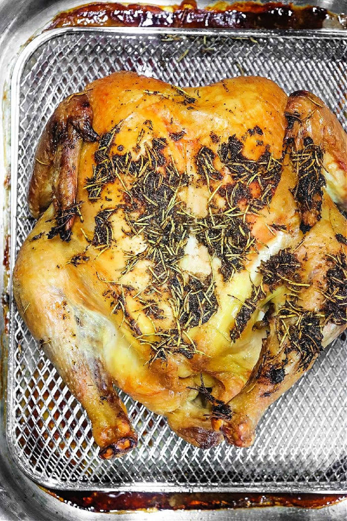Whole roasted chicken with herbs on top, placed in a metal air fryer basket—an easy way to enjoy the flavor of Frozen Chicken in Oven, now crisped to perfection.