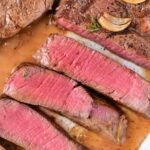 Sliced medium-rare steak with garlic and seasoning on a plate, capturing the essence of how to cook beef tenderloin medallions to perfection.