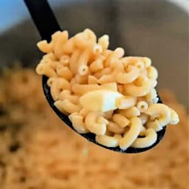 A spoonful of cooked elbow macaroni with a piece of butter, held over a pot of more macaroni—perfect for making creamy Ninja Foodi Butter Noodles.