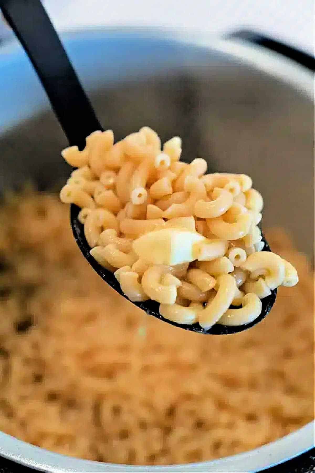 A spoonful of cooked elbow macaroni with a piece of butter, held over a pot of more macaroni—perfect for making creamy Ninja Foodi Butter Noodles.