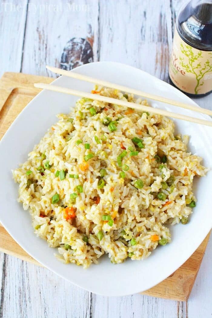 A plate of pressure cooker fried rice with chopsticks sits on a wooden board next to a bottle of soy sauce.