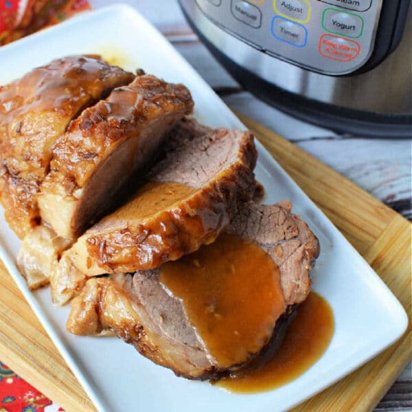 Sliced roast beef with gravy, made from a tender instant pot rump roast, served on a white plate next to an Instant Pot on a wooden board.