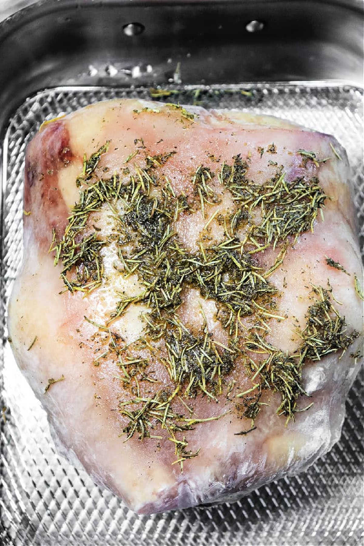 Raw lamb roast covered with herbs and seasonings in a metal roasting pan, ready to cook just like if you were preparing frozen chicken in oven for a hearty meal.
