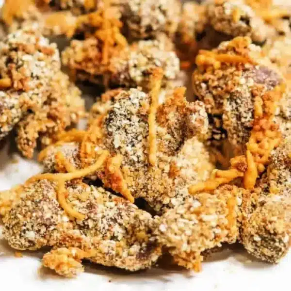 Close-up of a pile of breaded and fried chicken pieces. The chicken is coated in a textured breading, with some grated cheese visible on top and around the pieces.