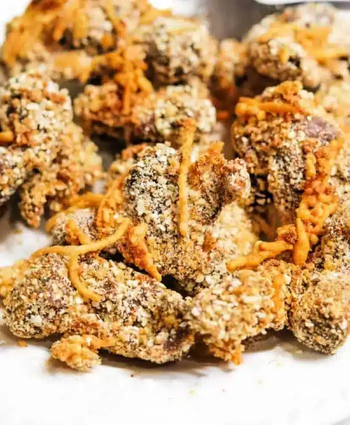 Close-up of a pile of breaded and fried chicken pieces. The chicken is coated in a textured breading, with some grated cheese visible on top and around the pieces.