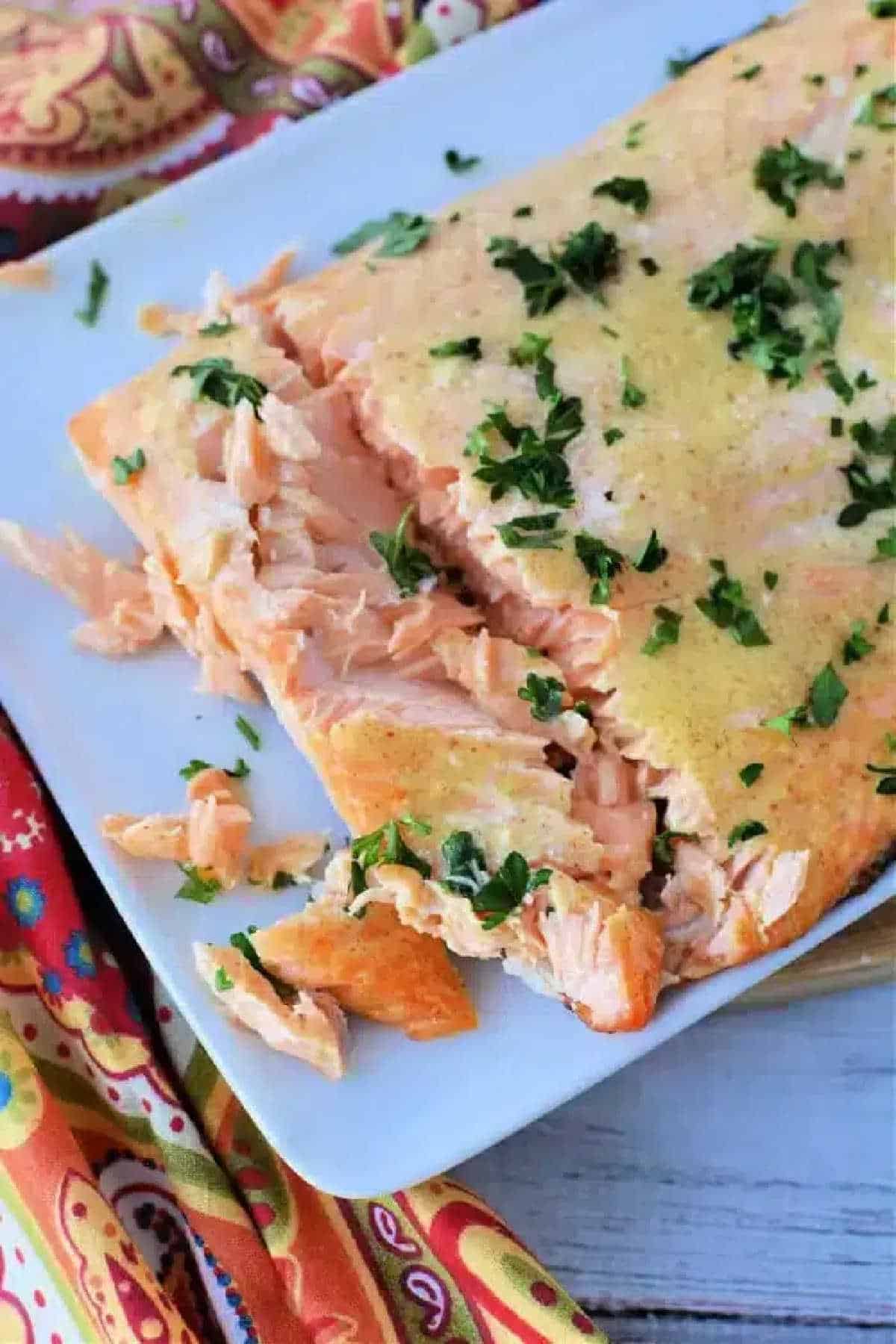 Frozen salmon in air fryer, cooked to perfection and garnished with chopped herbs on a white plate, partially flaked.