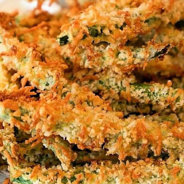 Crispy baked zucchini fries coated in golden breadcrumbs, stacked on a white plate, reminiscent of the irresistible crunch found in Air Fryer Green Bean Fries.