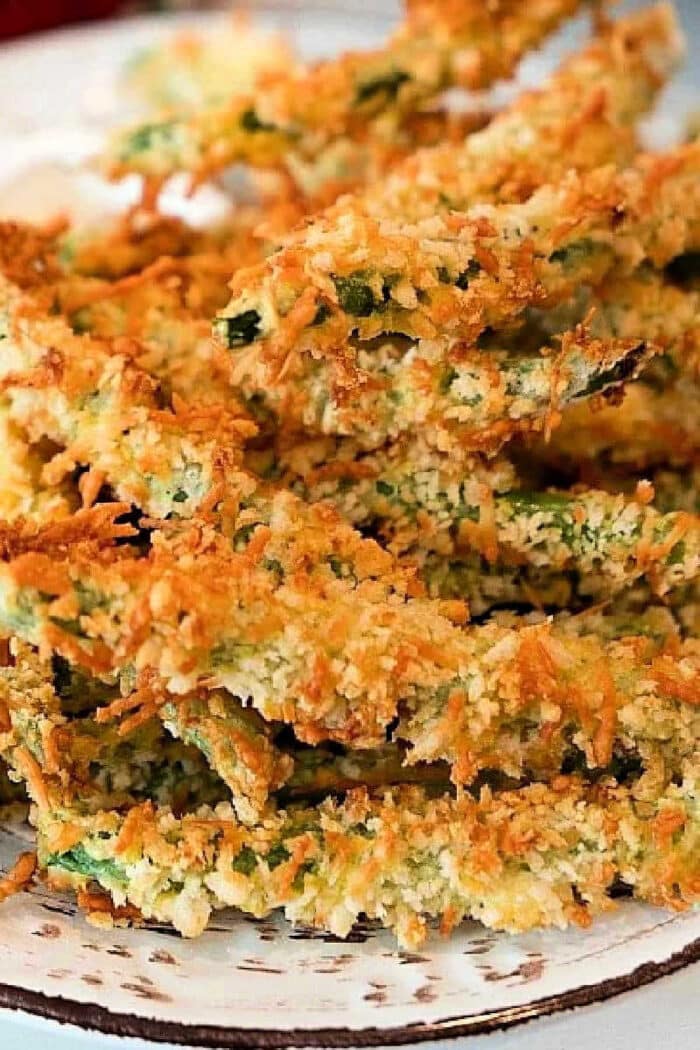 Crispy baked zucchini fries coated in golden breadcrumbs, stacked on a white plate, reminiscent of the irresistible crunch found in Air Fryer Green Bean Fries.