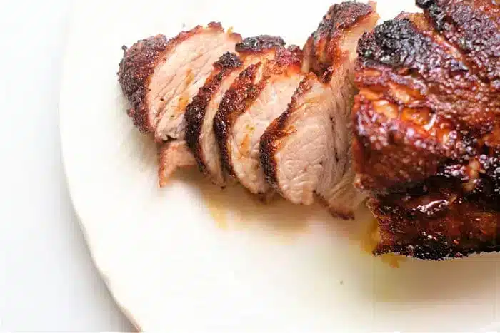 Sliced, grilled meat with a charred brown exterior served on a white plate. The interior of the air fryer pork roast appears tender and juicy.