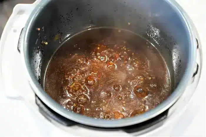 A close-up of a steaming pot on a stovetop reveals a dark, bubbling liquid, brimming with spices. The well-worn pot cradles a savory beef arm roast recipe, its contents simmering energetically.