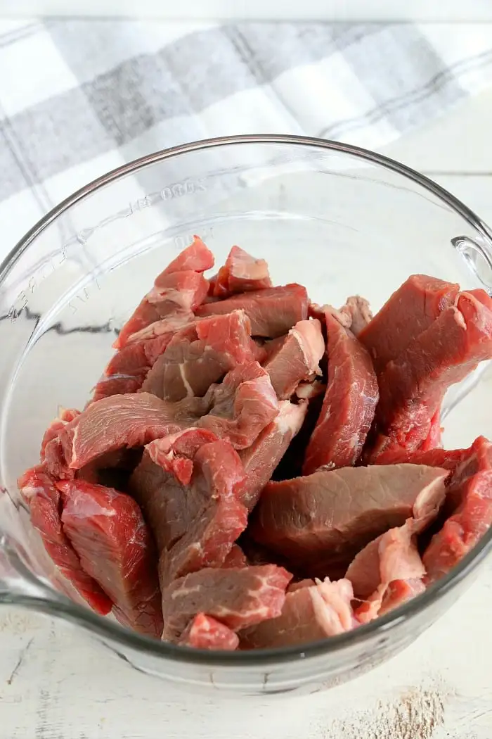 A clear glass bowl filled with raw, thinly sliced beef pieces, perfect for making air fryer beef jerky.