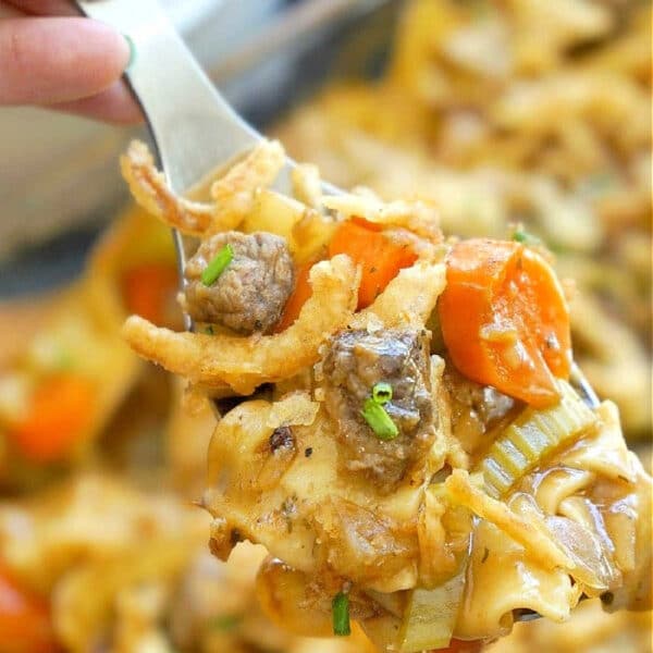 A fork holding a bite of easy beef stew casserole with noodles, beef, carrots, celery, and crispy onions.